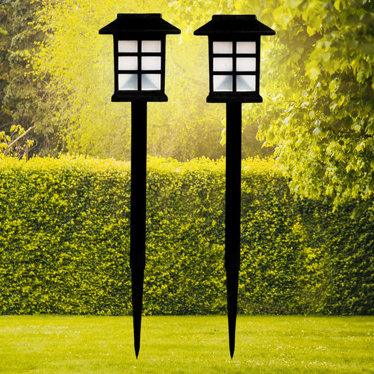 A pair of sleek black solar garden lights illuminating a lush green lawn at dusk.