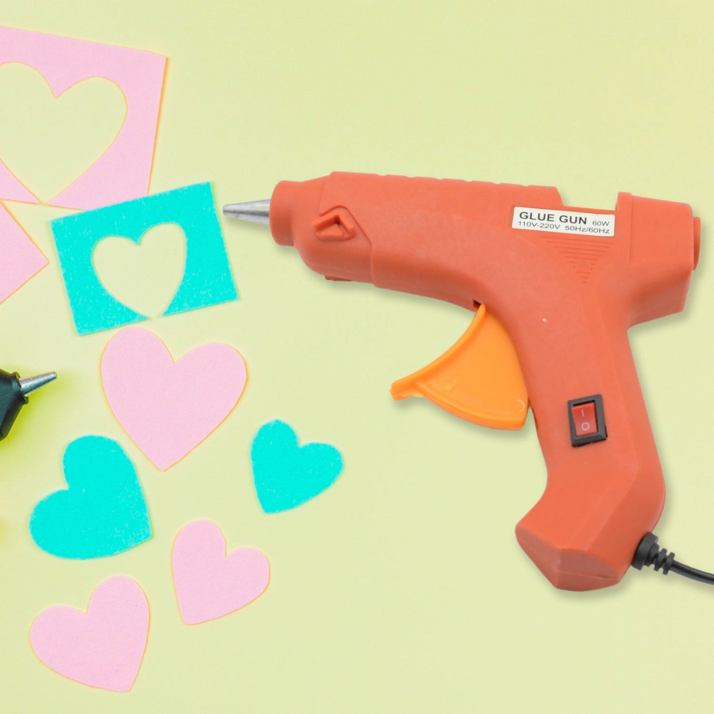 An electric hot melt glue gun with its power cord and a bundle of glue sticks on a clean surface.