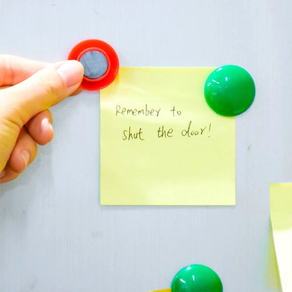 Colorful board magnets holding papers on a white magnetic surface.
