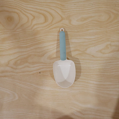 A white plastic measuring spoon demonstrating its use as a bag clip on a food bag.