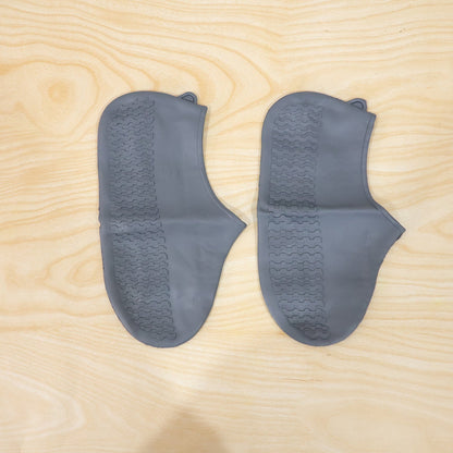 Waterproof silicone shoe covers being worn by a person walking through a muddy park.